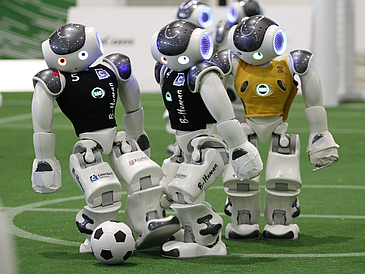Drei Roboter spielen Fußball.