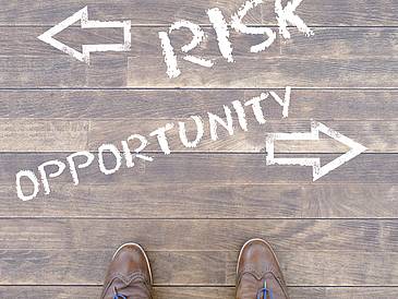 Ein Mann schaut auf die Wörter "Risk" und "Opportunity" herab, die mit Kreide auf den Boden geschrieben wurden