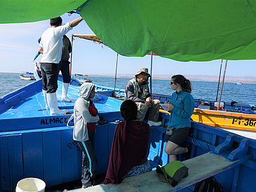 Auf einem Fischerboot interviewt eine Wissenschaftlerin eine Gruppe von Fischer:innen