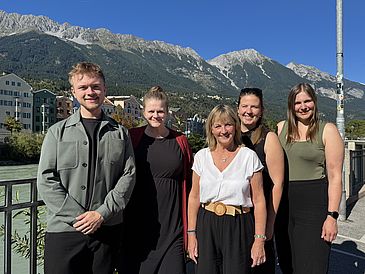 Fünf Personen stehen an einem Fluss vor einem Bergpanorama.