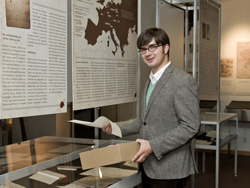 Mann mit kleinem Pappkarton in der Hand vor Museumsvitrine