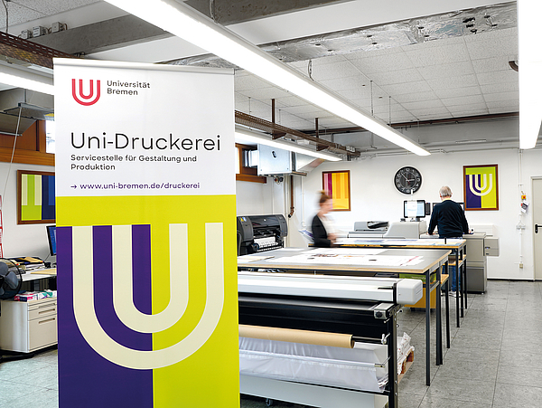 Blick in die Uni-Druckerei mit großen Tischen und diversen Maschinen