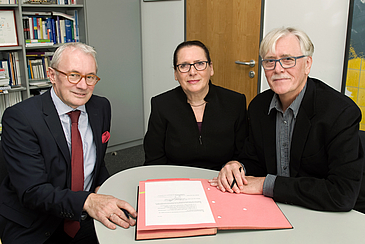 Zwei Männer und eine Frau unterzeichnen den Vertrag