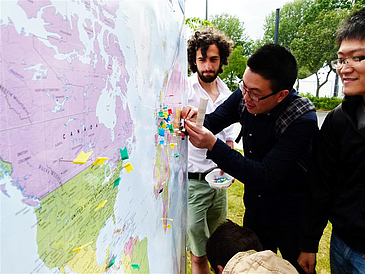 Internationale Studierende markieren Orte auf einer Weltkarte.