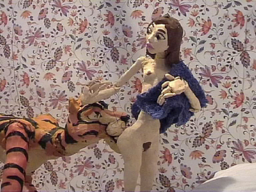 filmstill mit Puppen: stehende nackte Frau, der ein Tiger den Po leckt