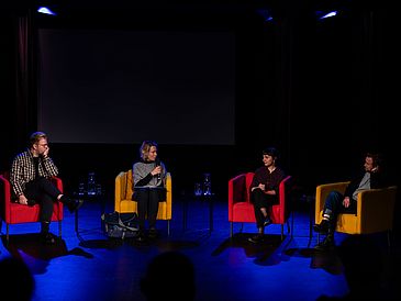 Vier Personen auf dem Podium in bunten Sesseln