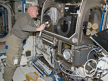 Astronaut Scott Kelly beim Einbau des ersten Versuchsmodells in die Microgravity Science Glovebox auf der ISS