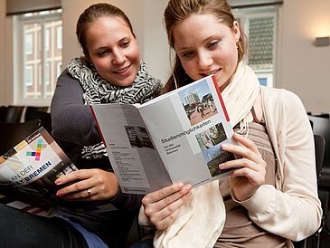 Zwei junge Frauen lesen eine Broschüre.