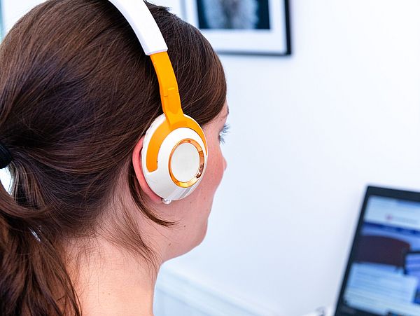Eine Frau mit Kopfhörer sitzt vor einem aufgeklapptem Laptop