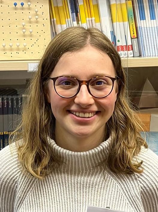 Eine Person steht lächelnd vor einer Vitrine mit Schulbüchern