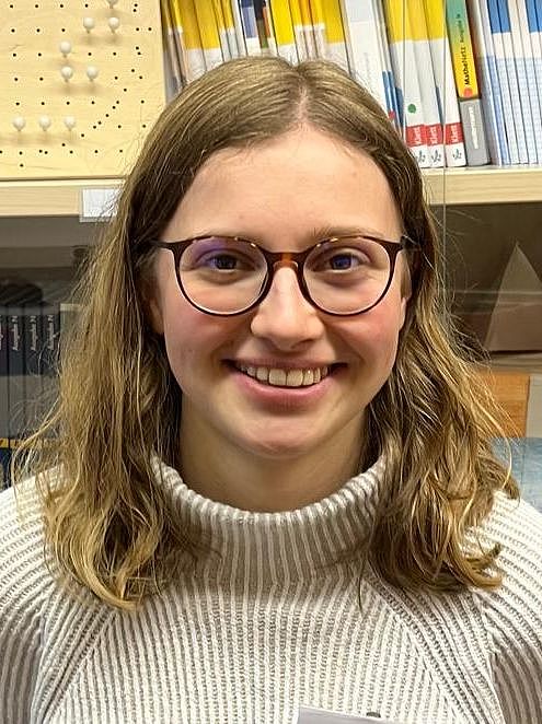 Eine Person steht lächelnd vor einer Vitrine mit Schulbüchern