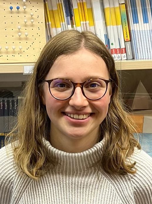 Eine Person steht lächelnd vor einer Vitrine mit Schulbüchern