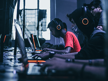 junge Männer spielen Videospiele in einer Reihe, Orangene Akzente in dunklem Gesamtambiente