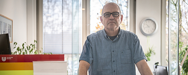 Dirk Dietzel stands behind a counter and looks into the camera through a plexiglass pane.