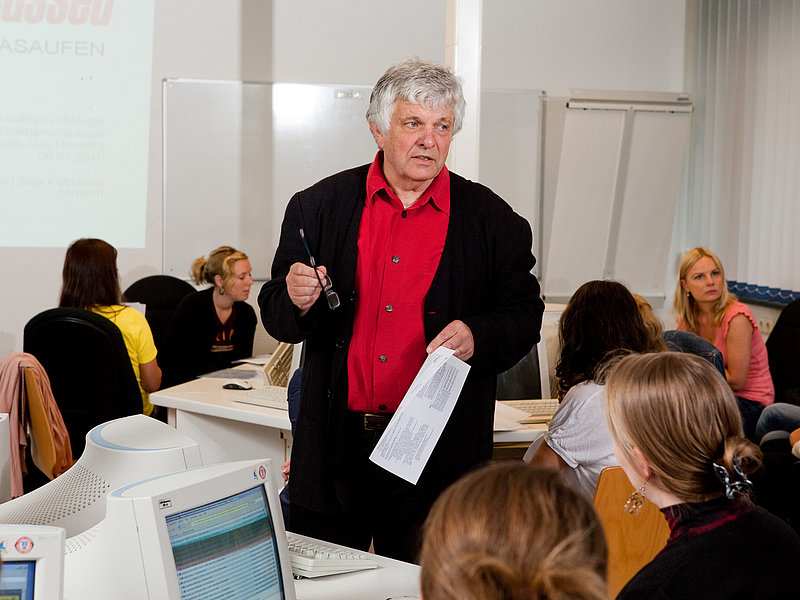 Ein Lehrender im Gespräch mit Studierenden in einem Seminarraum.