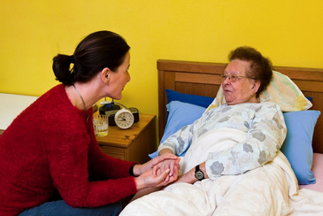 A woman in her bed, caregiver holds her hand