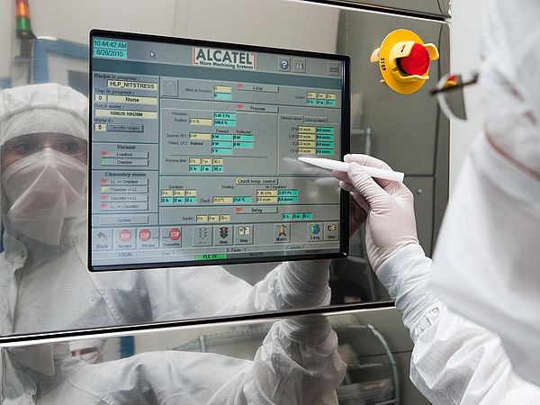 A person in protective clothing operates the touchscreen of a laboratory device.
