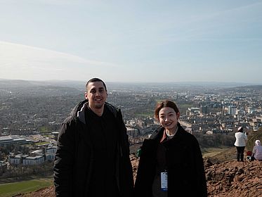 Nima and Izzi infront of a beautiful landscape of edinburgh