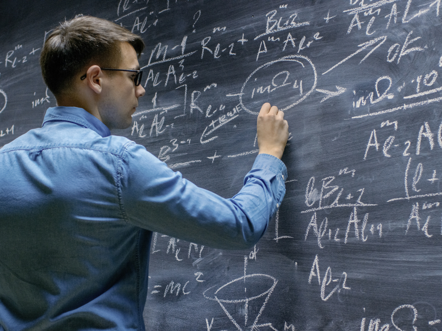 Mann schreibt mathematische Formeln an eine Tafel.
