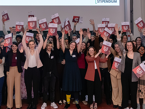 Stipendiat:innen jubeln mit Mappen in der Hand.