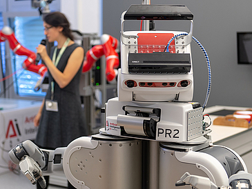 Roboter PR2, im Hintergrund eine Frau mit Mikrofon