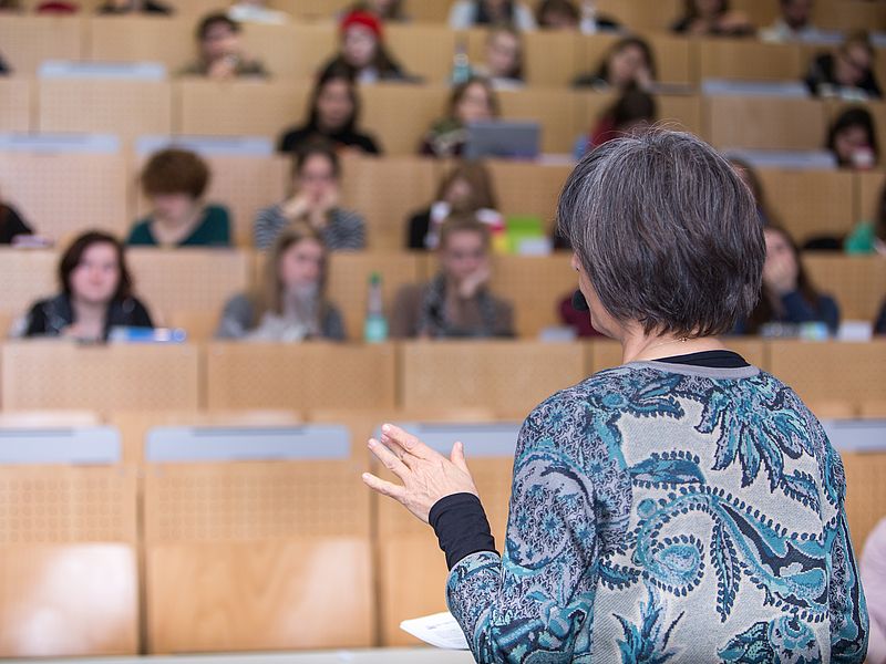 A lecturer speaks to an audience in a packed lecture hall.