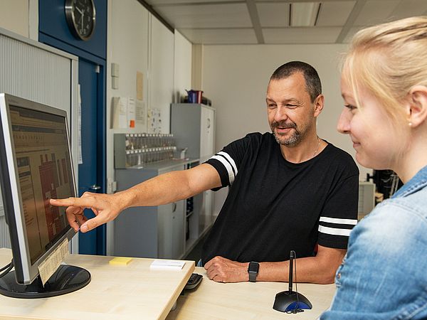 Zwei Personen im Gespräch an einem Computerarbeitsplatz.