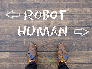 Ein Mann schaut auf die Wörter "Robot" und "Human" herab, die mit Kreide auf den Boden geschrieben wurden
