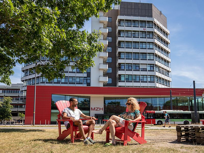 Two people on red chairs in front of the MZH.