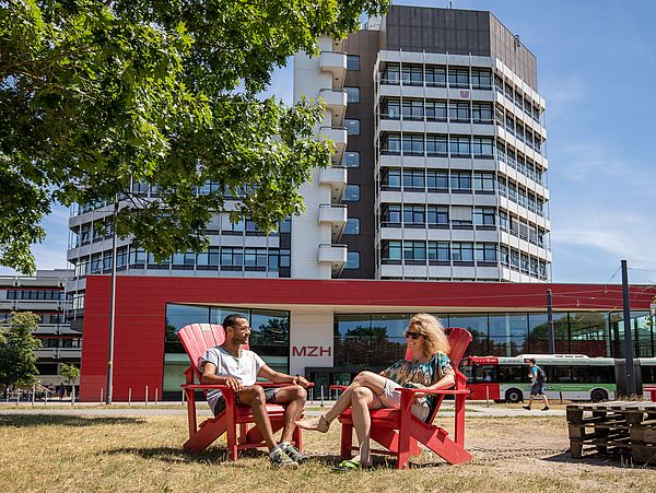 Zwei Personen auf roten Stühlen vor dem MZH.