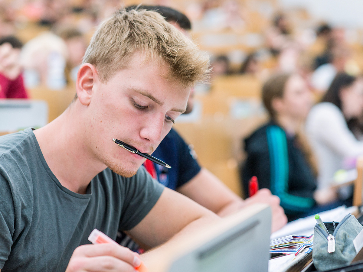 Ein Studierender macht sich im vollen Hörsaal Notizen.