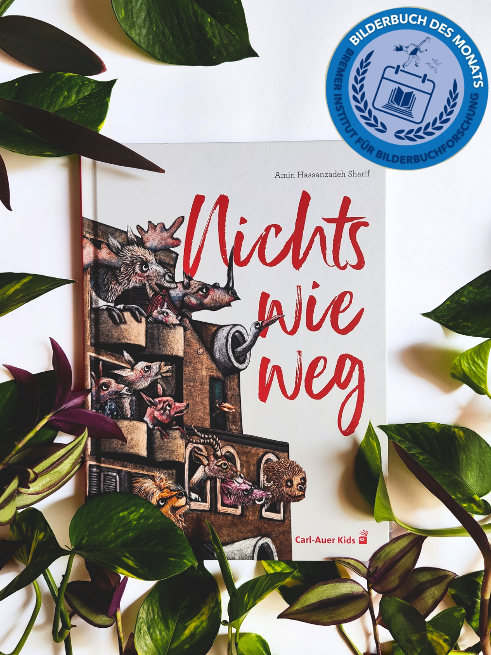 Das Bild zeigt das Cover des Bilderbuchs umrahmt von Blättern und dem Bilderbuch des Monats-Logo oben rechts.