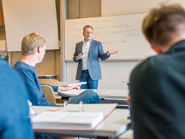 Ein Lehrender spricht vor Zuhörern in einem Seminarraum.