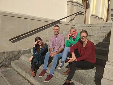 Team des Projekts (vier Personen) auf einer Treppe in der Sonne sitzend.