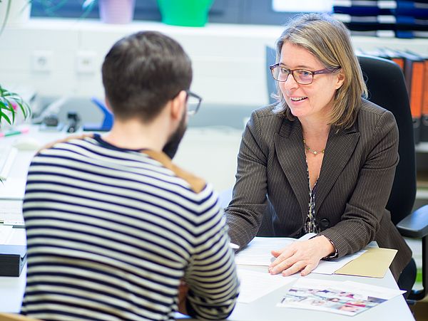Zwei Personen im Gespräch an einem Bürotisch.