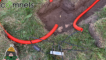 A hole has been dug in the lawn. You can see a soil moisture sensor, a few empty conduits, some cables, etc. In the next step, the sensor will be placed in the hole.