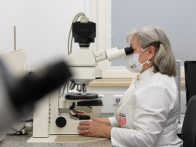 Employee in a gown in front of a microscope.