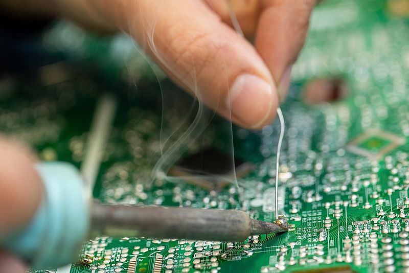 One person solders a circuit board.