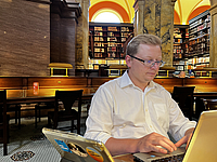 Konrad Szocik working on a laptop while sitting in an old library.