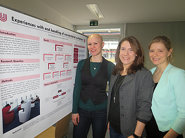 Drei junge Frauen vor einer Plakatwand während einer Konferenz.