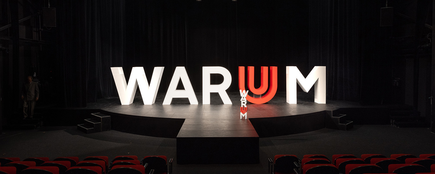 Ein WARUM aus dreidimensionalen Buchstaben zusammengestellt, platziert auf einer Bühne.