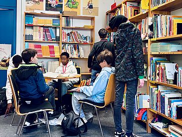 Die Jungen beim Auswählen eines interessanten Bilderbuches am Tisch und vorm Regal