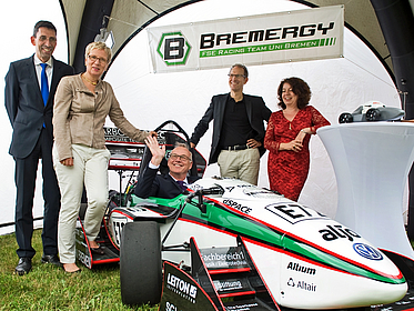 Mann sitzt im Rennwagen. Vier Personen stehen dabei.