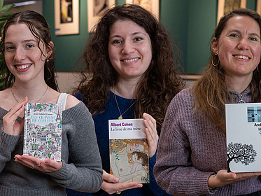 Drei Studentinnen halten jeweils ein Buchcover in die Kamera