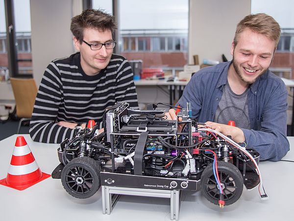 Zwei Personen arbeiten an einem selbstfahrenden Modellauto.