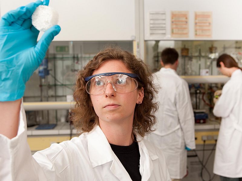 A person wearing safety goggles looks at an object in their hand.