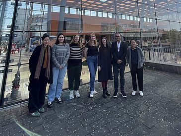 Women and one man in front of main university glass hall