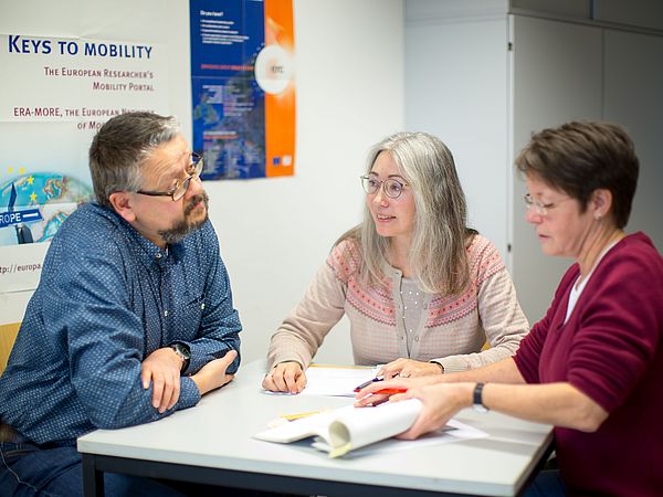 Drei Personen im Gespräch an einem Tisch.
