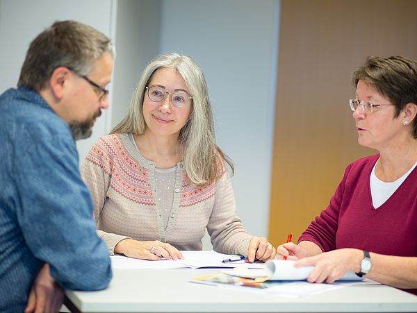Three people in conversation at a table.