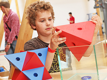 Kind hält Exponat in einem Mitmachmuseum für Mathematik in der Hand